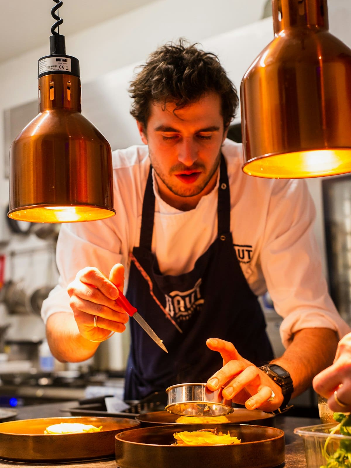 A chef plating dishes under heat lamps during service